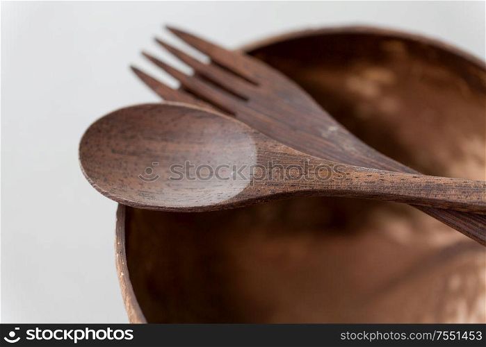 recycling, tableware and eco friendly concept - close up of coconut bowl with brown wooden spoon and fork on table. close up of coconut bowl, wooden spoon and fork