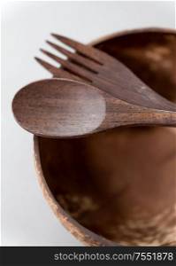recycling, tableware and eco friendly concept - close up of coconut bowl with brown wooden spoon and fork on table. close up of coconut bowl, wooden spoon and fork