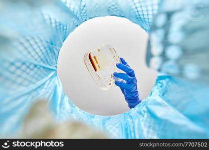 recycling, waste sorting and sustainability concept - hand in glove throwing disposable plastic food container into trash can. hand throwing plastic container into trash can