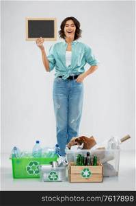 recycling, waste sorting and sustainability concept - happy smiling young woman with chalkboard, plastic and glass bottles, paper and metal tin cans in boxes over grey background. happy woman sorting paper, metal and plastic waste