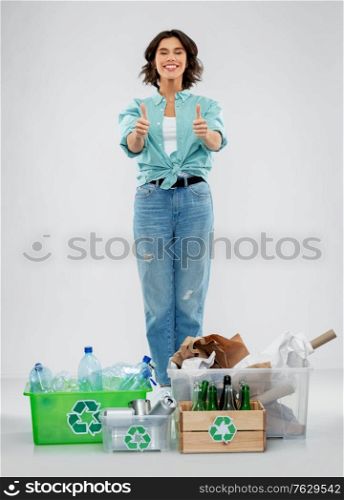 recycling, waste sorting and sustainability concept - happy smiling young woman with plastic and glass bottles, paper and metal tin cans in boxes showing thumbs up over grey background. happy woman sorting paper, metal and plastic waste