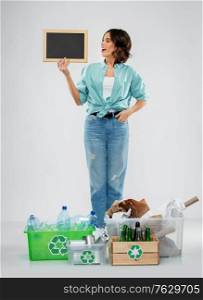 recycling, waste sorting and sustainability concept - happy smiling young woman with chalkboard, plastic and glass bottles, paper and metal tin cans in boxes over grey background. happy woman sorting paper, metal and plastic waste