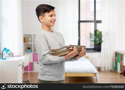 recycling, waste sorting and sustainability concept - smiling boy holding heap of paper magazines over home room on background. smiling boy with magazines sorting paper waste