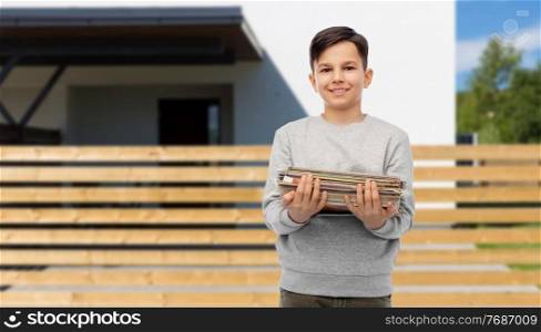 recycling, waste sorting and sustainability concept - smiling boy holding heap of paper magazines over house background. smiling boy with magazines sorting paper waste