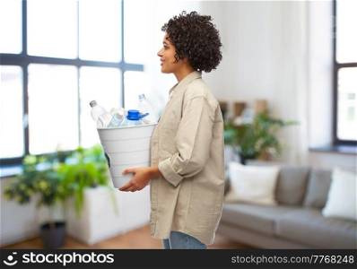 recycling, waste sorting and sustainability concept - smiling woman holding recycle bin with plastic bottles over home background. smiling young woman sorting plastic waste