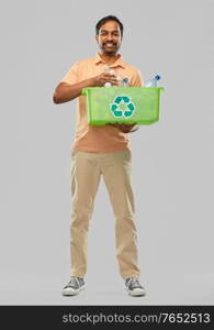 recycling, waste sorting and sustainability concept - smiling young indian man in striped t-shirt holding box with plastic bottles over grey background. smiling young indian man sorting plastic waste