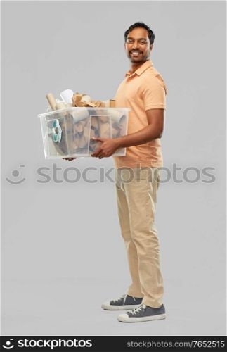 recycling, waste sorting and sustainability concept - smiling young indian man in polo t-shirt holding paper garbage in plastic box over grey background. smiling young indian man sorting paper waste
