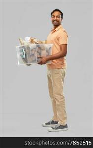 recycling, waste sorting and sustainability concept - smiling young indian man in polo t-shirt holding paper garbage in plastic box over grey background. smiling young indian man sorting paper waste