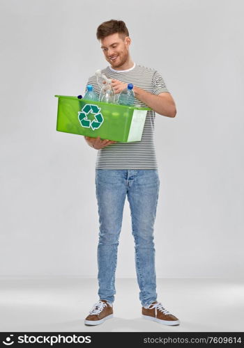 recycling, waste sorting and sustainability concept - smiling young man in striped t-shirt holding box with plastic bottles over grey background. smiling young man sorting plastic waste