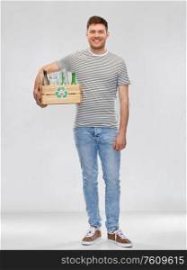 recycling, waste sorting and sustainability concept - smiling young man in striped t-shirt holding wooden box with glass bottles and jars over grey background. smiling young man sorting glass waste