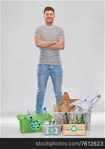 recycling, waste sorting and sustainability concept - smiling young man in striped t-shirt with plastic and glass bottles, papers and metal tin cans in boxes over grey background. smiling man sorting paper, metal and plastic waste