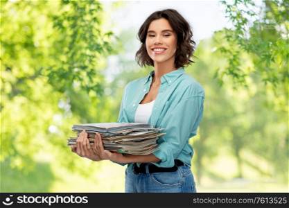 recycling, waste sorting and sustainability concept - smiling young woman holding heap of paper magazines over green natural background. smiling young woman sorting paper waste