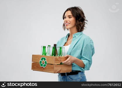 recycling, waste sorting and sustainability concept - smiling young woman holding wooden box with glass bottles and jars over grey background. smiling young woman sorting glass waste