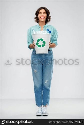 recycling, waste sorting and sustainability concept - smiling young woman in striped t-shirt holding trash bin with plastic bottles over grey background. smiling young woman sorting plastic waste