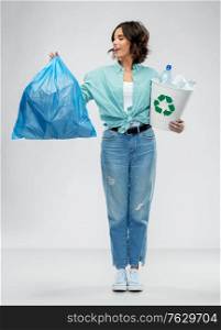 recycling, waste sorting and sustainability concept - smiling young woman in striped t-shirt holding rubbish bin with plastic bottles and trash bag over grey background. smiling woman sorting plastic waste with trash bag