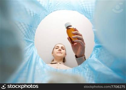 recycling, waste sorting and sustainability concept - woman throwing glass bottle with expired medicine into trash can. woman throwing old medicine into trash can