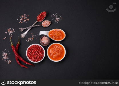 Red adjika sauce or ketchup with spices and herbs on a dark concrete background