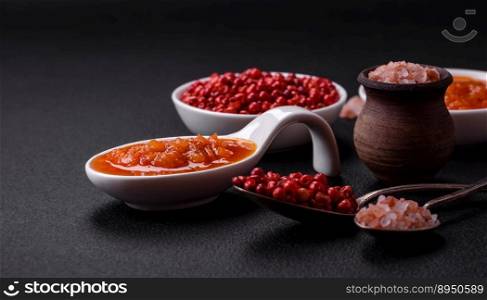 Red adjika sauce or ketchup with spices and herbs on a dark concrete background
