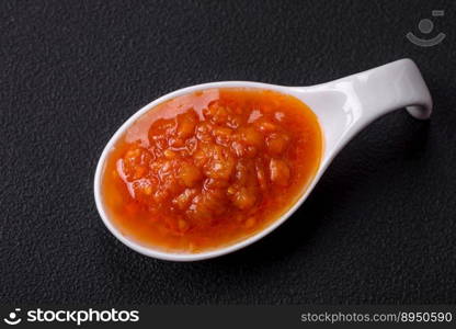 Red adjika sauce or ketchup with spices and herbs on a dark concrete background