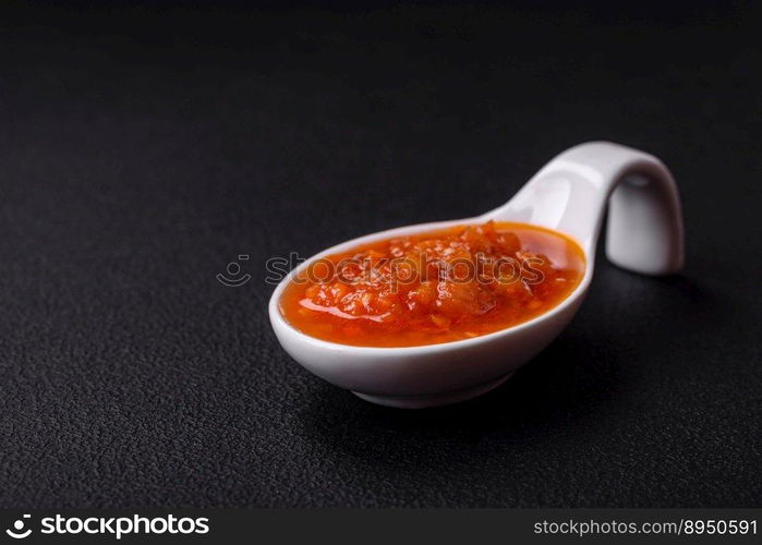 Red adjika sauce or ketchup with spices and herbs on a dark concrete background