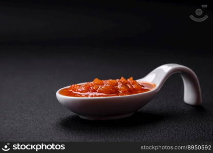 Red adjika sauce or ketchup with spices and herbs on a dark concrete background