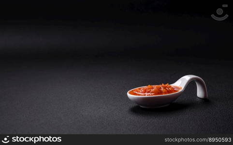 Red adjika sauce or ketchup with spices and herbs on a dark concrete background