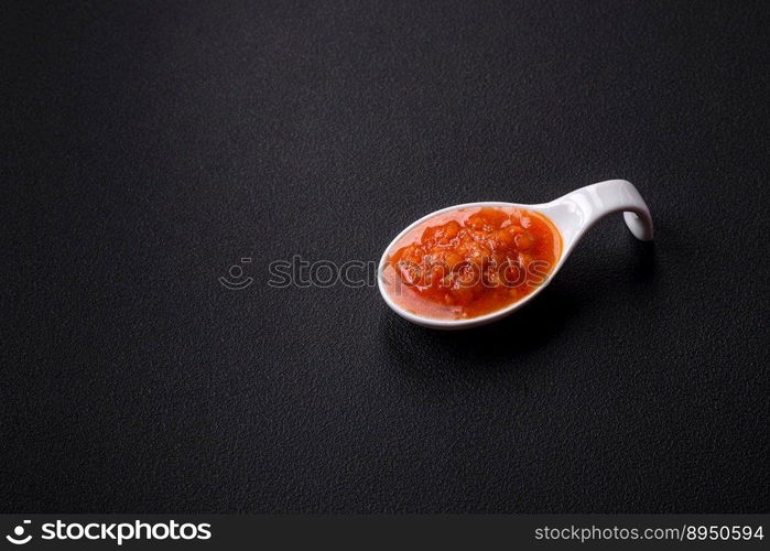 Red adjika sauce or ketchup with spices and herbs on a dark concrete background