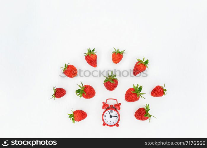 Red alarm clock and flying scattering strawberries berry on white background. Top view, flat lay, copy space. Concept diet and detox time or summer menu time. Template for text, design, invitation.. Red alarm clock and flying scattering strawberries berry on white background. Top view, flat lay, copy space. Concept diet and detox time or summer menu time. Template for text, design, invitation