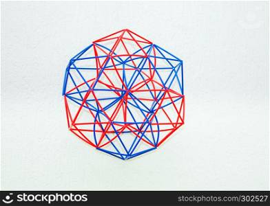 Red and blue handmade three-dimensional model of geometric solid on a white textured background.. Coloured Handmade Dimensional Model Of Geometric Solid