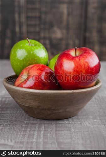 Red and green apples in wooden bowl on wooden board