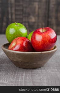 Red and green apples in wooden bowl on wooden board