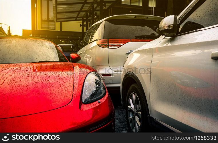 Red and silver car parked on outdoor concrete parking lot of the hotel, home, or apartment. Electric or hybrid car technology. Parking space for rent business. Raindrops on sport car and SUV car.