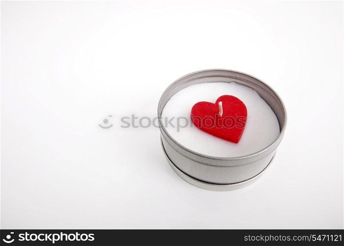 Red and white candle with heart shape in container against white background