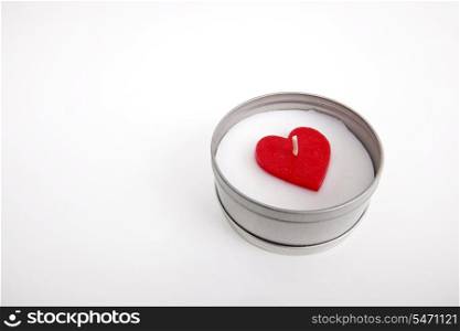Red and white candle with heart shape in container against white background