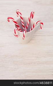 Red and white candy canes in a cup on a gray wooden background