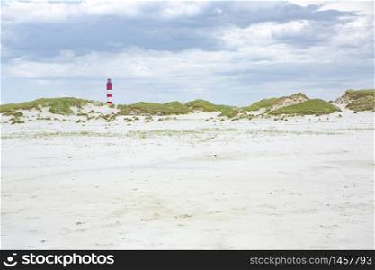 Red and white lighthouse on the hill viewed from low angle with green grass and white sand dunes in foreground on a sunny day in Amrum, Germany, Schleswig-Holstein