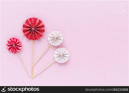 Red and white paper fan with wooden stick on pink background for party decoration