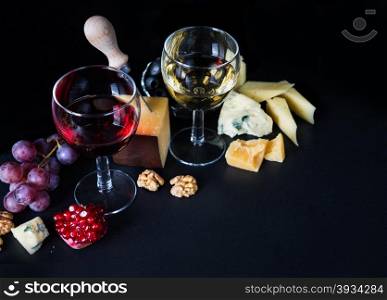Red and white wine, cheese, pomegranate and grapes on a black background