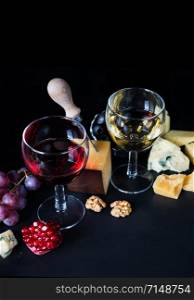 Red and white wine, cheese, pomegranate and grapes on a black background