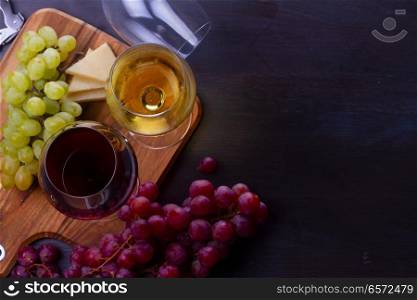 Red and wite wine in glasses with grape fruit, top view scene, copy space on dark wooden table. Glass of red and white wine