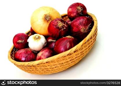 Red and yellow onions in a wicker basket with a single bulb of garlic. Basket Of Onions
