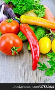 Red and yellow tomatoes, sweet and hot peppers, cucumbers, potatoes, carrots and parsley on a wooden boards background