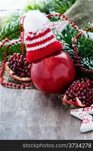 Red apple in hat and pomegranate with festive decorations over wooden background, selective focus, copy space