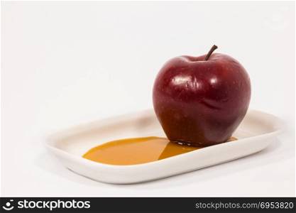Red apple on white plate with honey isolated on a white background. Symbols of Jewish New Year - Rosh Hashanah.