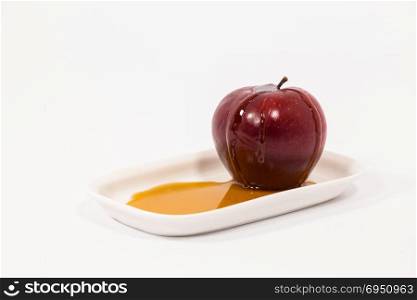Red apple with drops of honey on white plate with honey isolated on a white background. Symbols of Jewish New Year - Rosh Hashanah.