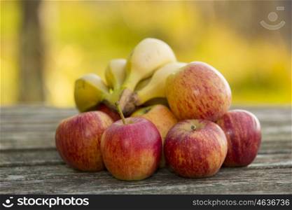 red apples and bananas on a wooden table, on green outdoor background