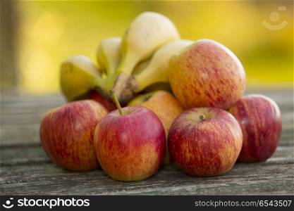 red apples and bananas on a wooden table, on green outdoor background. apples and bananas