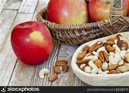 red apples and nuts (cashew, walnut, almond, Brazilian) in rustic setting (primitive wooden bowl and wicker basket over grunge painted wood surface)