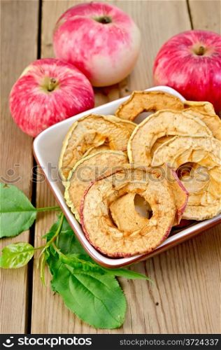 Red apples fresh and dried in a bowl, green leaves against wooden boards