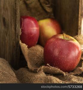 Red apples in rustic setting with old wooden box and hessian sack
